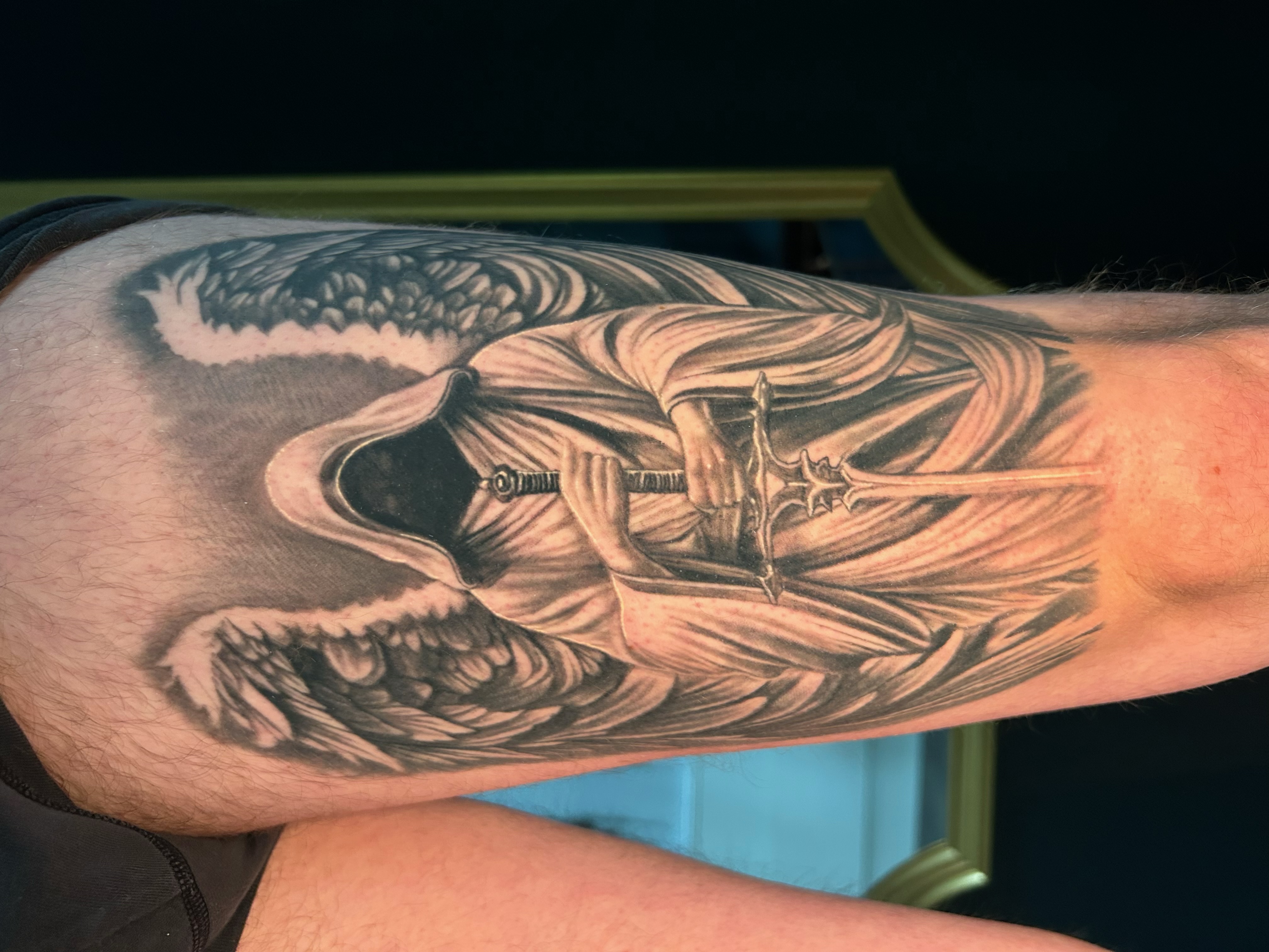 Black & Grey Tattoo mit geflügelter Figur und Schwert am Unterarm