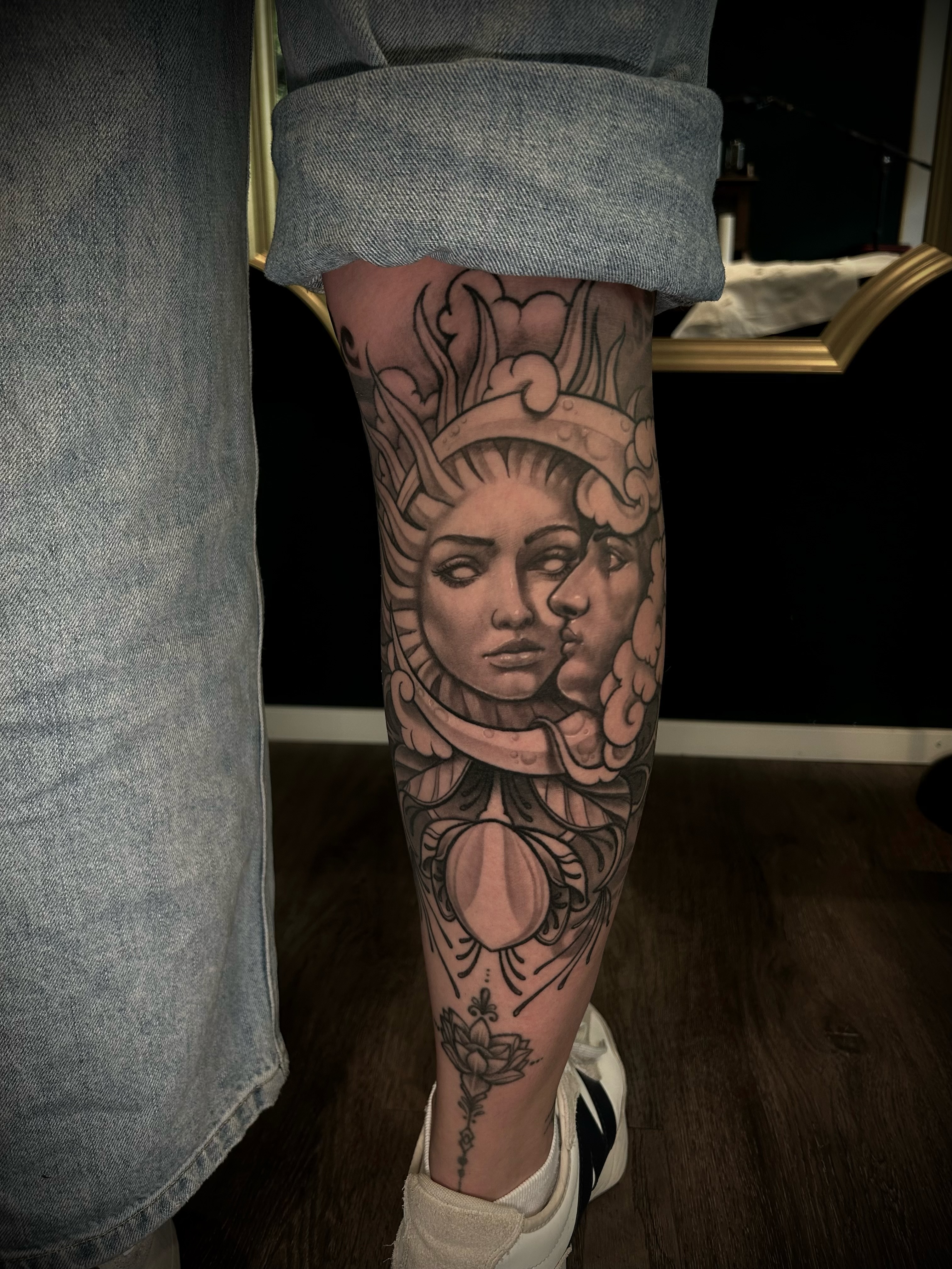 Custom-Tattoo mit Sonnen- und Mondgesicht sowie Krone am Unterschenkel